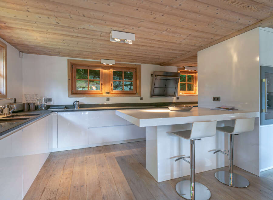 Modern kitchen with white cabinets and wooden ceiling.