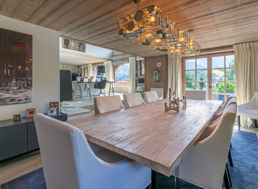 This stunning chalet boasts a spacious dining area with a rustic wooden table, complemented by elegant white chairs and a unique chandelier.