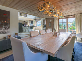 This stunning chalet boasts a spacious dining area with a rustic wooden table, complemented by elegant white chairs and a unique chandelier.