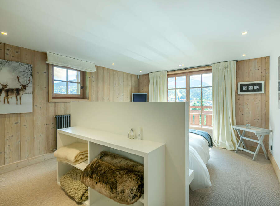 This stunning bedroom boasts a cozy and luxurious atmosphere, featuring a plush carpet, a built-in shelving unit perfect for storing blankets, and large windows offering breathtaking mountain views.