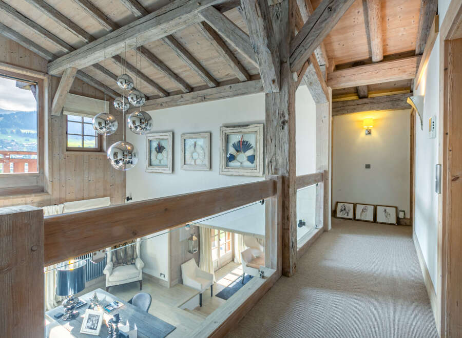 This stunning chalet boasts a breathtaking view and unique architectural details, including exposed wooden beams and a glass-walled upper hallway.