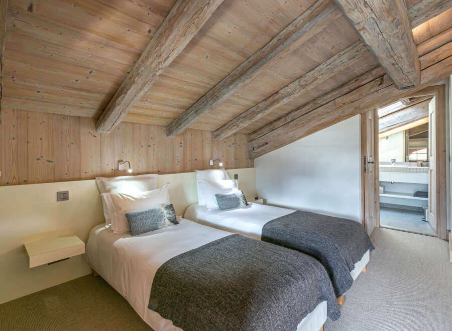 Cozy chalet bedroom with twin beds, exposed wooden beams, and a neutral color palette.