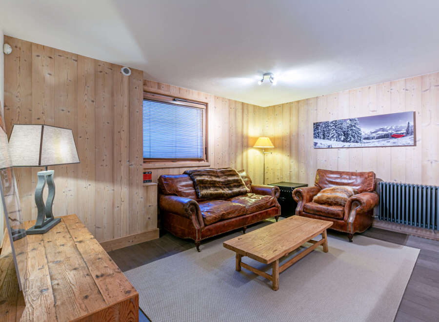 Cozy mountain chalet living room with leather sofas, wooden walls, and a rustic coffee table.