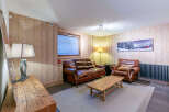 Cozy mountain chalet living room with leather sofas, wooden walls, and a rustic coffee table.