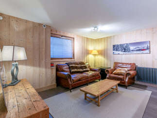 Cozy mountain chalet living room with leather sofas, wooden walls, and a rustic coffee table.