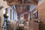 Rustic mountain chalet with exposed wooden beams, large windows offering stunning views, and a cozy living area featuring a comfortable sofa and sheepskin rug.
