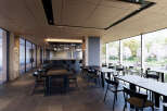 This modern restaurant boasts a sleek design with floor-to-ceiling windows offering scenic views, complemented by dark wood ceilings and black furniture.