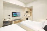 This modern hotel room features two twin beds with crisp white linens, a sleek wooden desk with a chair, and a flat-screen TV.