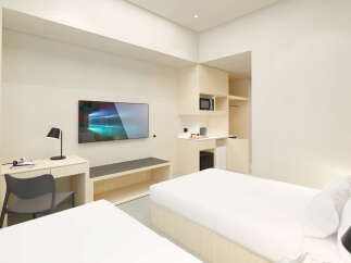 This modern hotel room features two twin beds with crisp white linens, a sleek wooden desk with a chair, and a flat-screen TV.