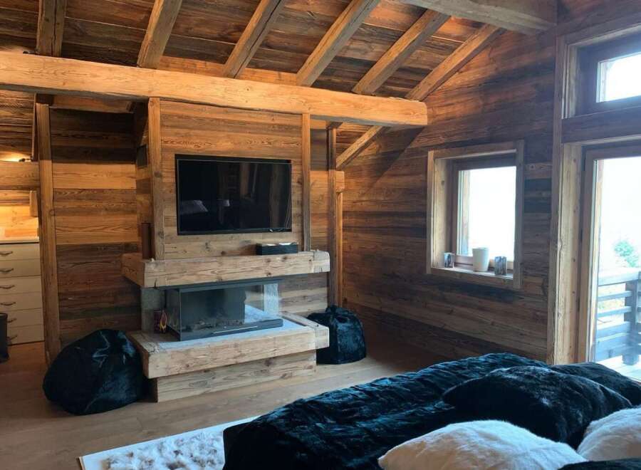 Rustic-chic bedroom with exposed wooden beams, a cozy fireplace, and plush bedding.