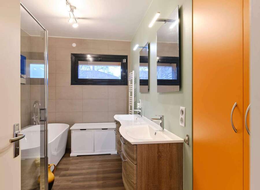 Modern bathroom with double vanity, freestanding bathtub, and bright orange storage cabinet.