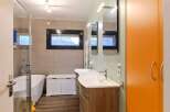 Modern bathroom with double vanity, freestanding bathtub, and bright orange storage cabinet.