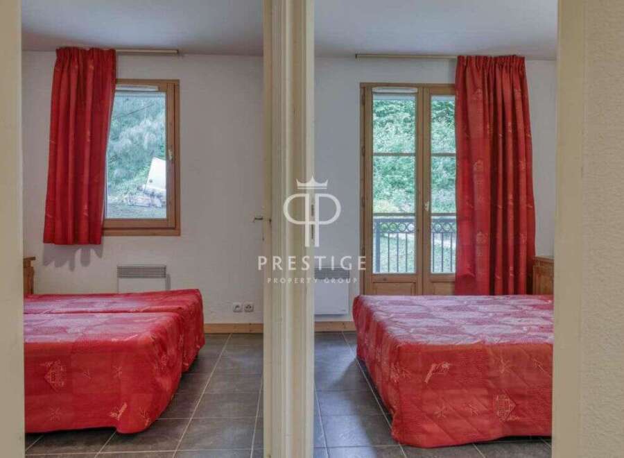 Discover a charming property featuring two cozy bedrooms, each adorned with vibrant red curtains and comfortable beds.