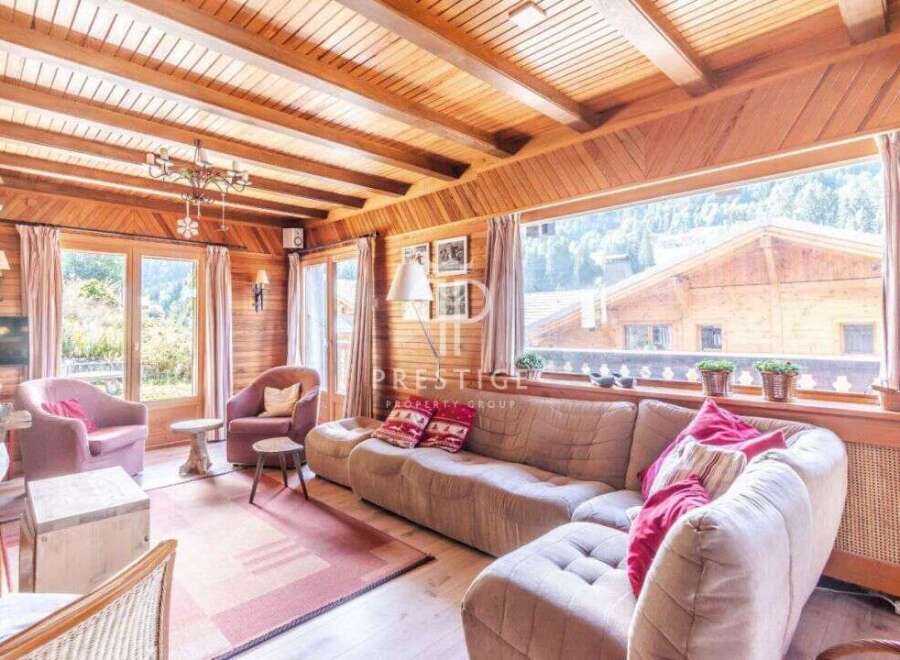 Experience the charm of this stunning property, featuring a cozy living room with a wooden ceiling and large windows.
