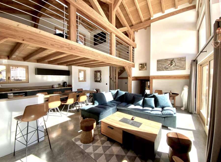 This stunning chalet boasts a spacious open-plan living area with high ceilings and exposed wooden beams, creating a warm and inviting atmosphere.