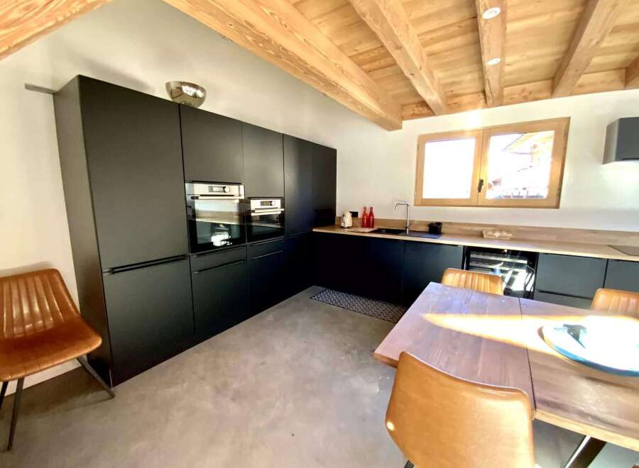 Modern kitchen with dark cabinetry, wooden beams, and concrete flooring.