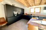 Modern kitchen with dark cabinetry, wooden beams, and concrete flooring.