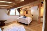 Cozy chalet bedroom with exposed wooden beams, a comfortable bed, and a fluffy rug.