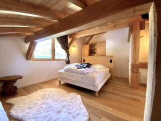 Cozy chalet bedroom with exposed wooden beams, a comfortable bed, and a fluffy rug.