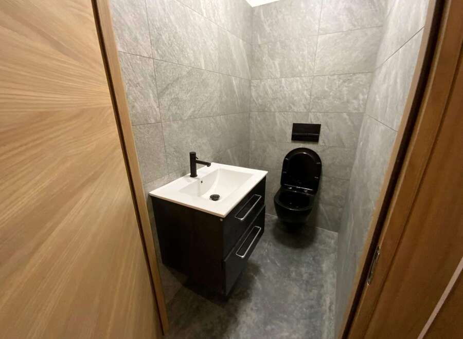 Modern bathroom with black toilet and vanity, and gray stone tile.