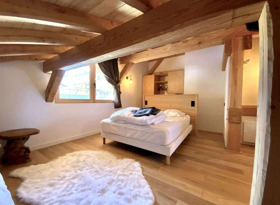 Cozy chalet bedroom with exposed wooden beams, a comfortable bed, and a fluffy rug.
