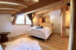 Cozy chalet bedroom with exposed wooden beams, a comfortable bed, and a fluffy rug.