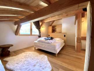 Cozy chalet bedroom with exposed wooden beams, a comfortable bed, and a fluffy rug.