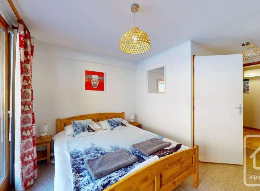 Cozy bedroom with wooden bed frame and winter-themed bedding, featuring a large window with red and white curtains.