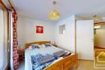 Cozy bedroom with wooden bed frame and winter-themed bedding, featuring a large window with red and white curtains.