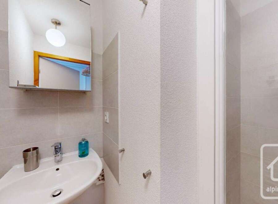 This modern bathroom boasts a sleek, corner sink with a mirrored medicine cabinet above, offering ample storage and counter space.