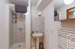 This charming bathroom boasts a modern shower enclosure with built-in shelving, a pedestal sink, and a heated towel rail for added convenience.