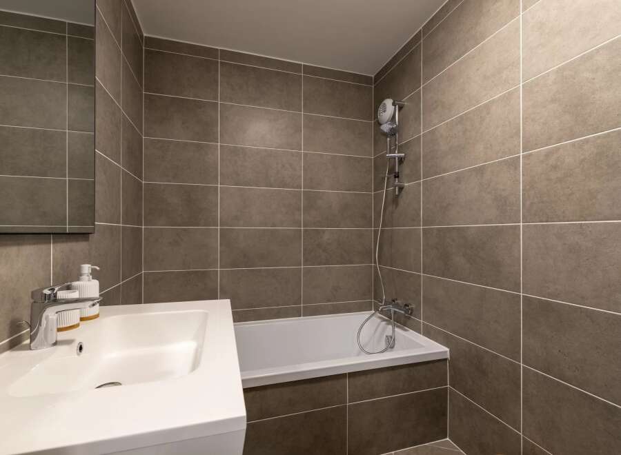 This modern bathroom features sleek, gray tiled walls and a pristine white sink and bathtub.