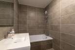 This modern bathroom features sleek, gray tiled walls and a pristine white sink and bathtub.