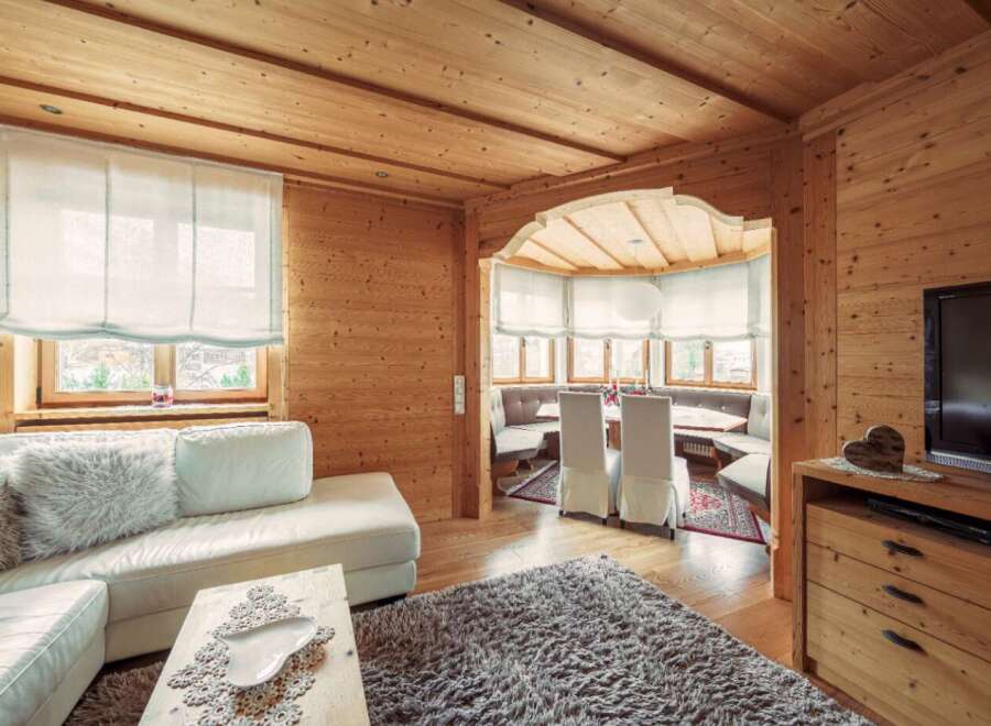 Cozy wooden chalet living room with comfy white sectional sofa, large flat-screen TV, and a charming dining area.