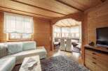 Cozy wooden chalet living room with comfy white sectional sofa, large flat-screen TV, and a charming dining area.
