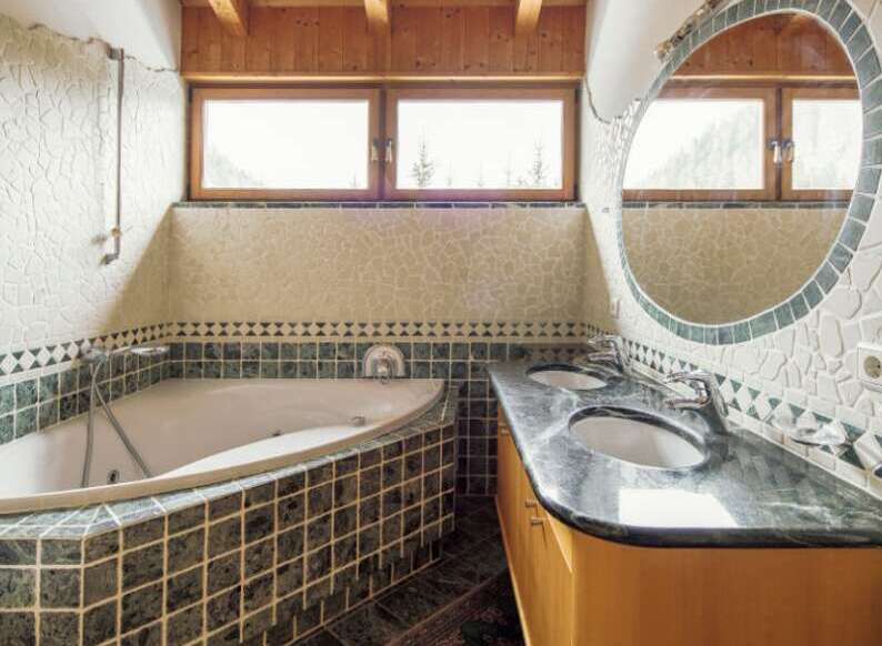 Luxurious bathroom with a corner jacuzzi tub and a large, round mirror.