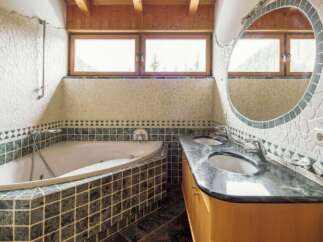 Luxurious bathroom with a corner jacuzzi tub and a large, round mirror.