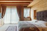Cozy mountain chalet bedroom with wooden beams, large windows, and a comfortable bed.