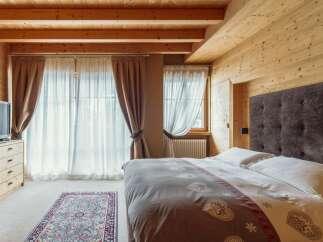 Cozy mountain chalet bedroom with wooden beams, large windows, and a comfortable bed.