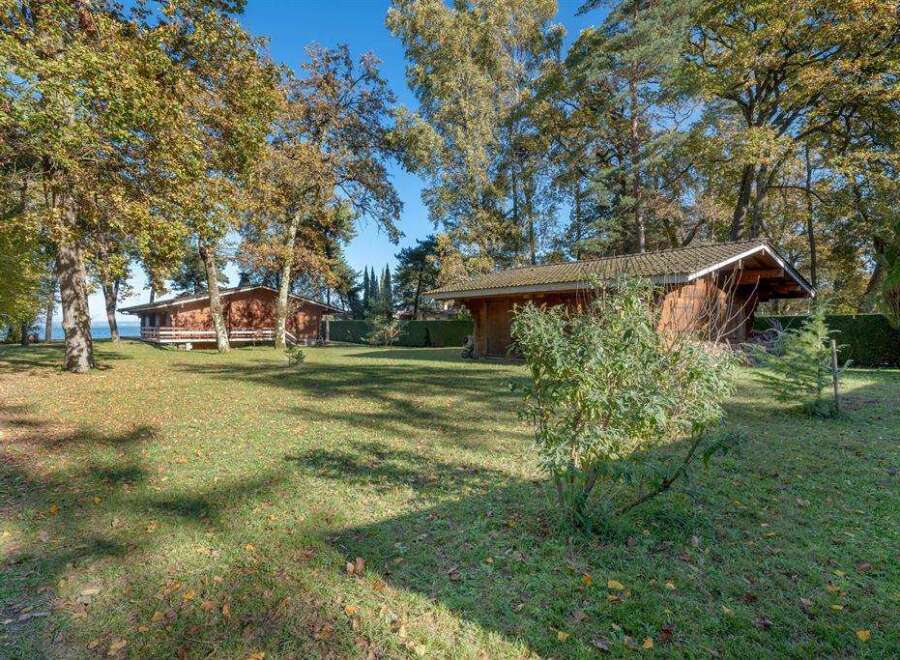 Discover this idyllic lakeside property featuring two charming wooden cabins nestled amongst mature trees.