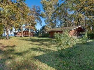 Discover this idyllic lakeside property featuring two charming wooden cabins nestled amongst mature trees.