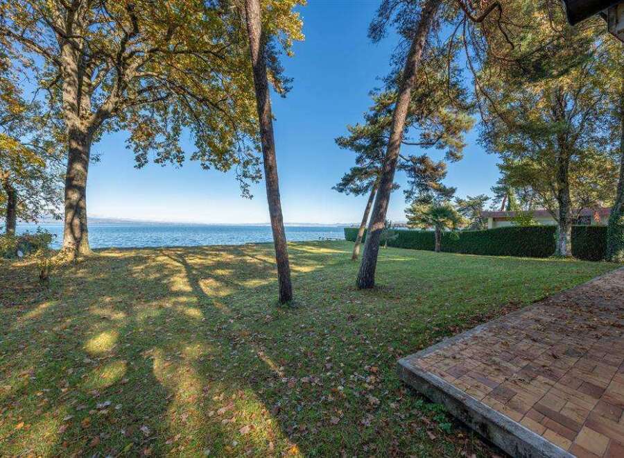 This stunning lakeside property boasts a spacious lawn, mature trees providing shade, and a brick patio perfect for outdoor entertaining.