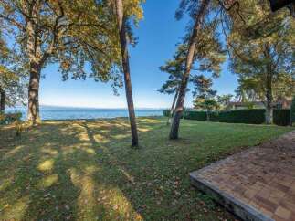This stunning lakeside property boasts a spacious lawn, mature trees providing shade, and a brick patio perfect for outdoor entertaining.