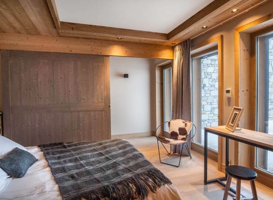 This stunning bedroom boasts a cozy and luxurious design, featuring a comfortable bed with a plush throw, a stylish cowhide chair, and a sleek wooden desk.