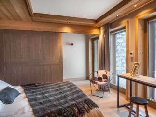 This stunning bedroom boasts a cozy and luxurious design, featuring a comfortable bed with a plush throw, a stylish cowhide chair, and a sleek wooden desk.