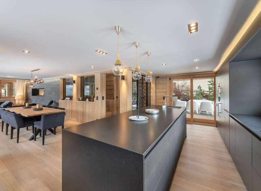 This stunning chalet boasts a spacious open-plan living area with a sleek, modern kitchen featuring a large island and high-end appliances.