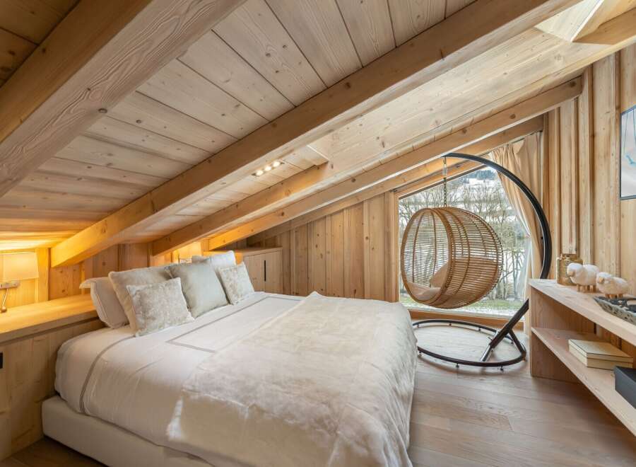 Cozy chalet bedroom with a king-size bed, wooden beams, and a window seat offering stunning views.