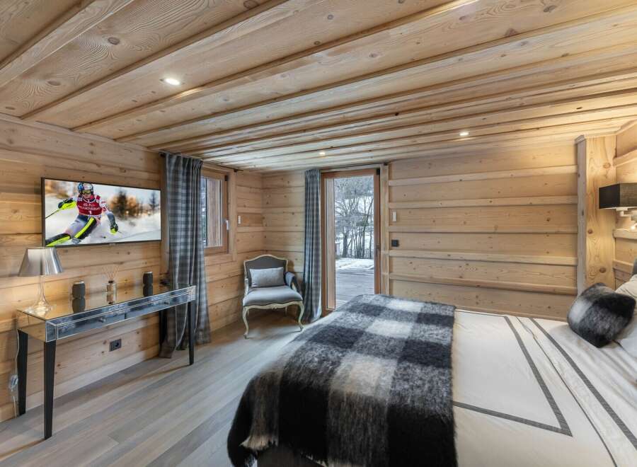 This stunning chalet bedroom boasts a cozy wooden interior, complete with a flat-screen TV and comfortable seating area.