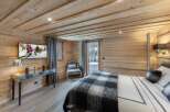 This stunning chalet bedroom boasts a cozy wooden interior, complete with a flat-screen TV and comfortable seating area.