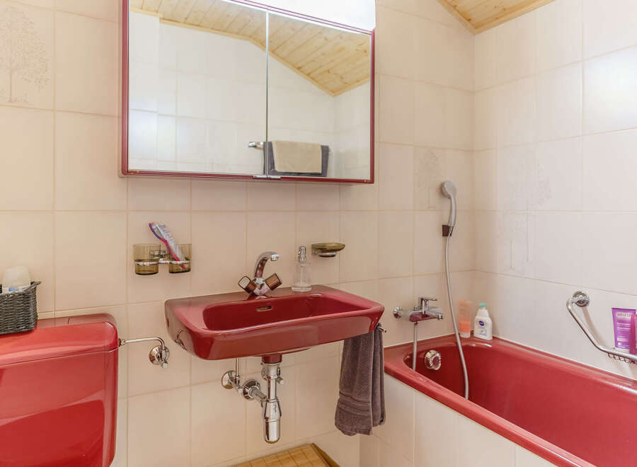 This charming bathroom features a vibrant red sink and bathtub, adding a pop of color to the space.